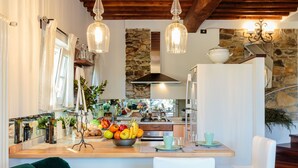 Una cocina con isla central, techo de madera, pared de piedra y lámparas colgantes.