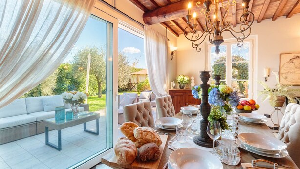 Un comedor con mesa de madera dispuesta para una comida, una araña y vistas al exterior.
