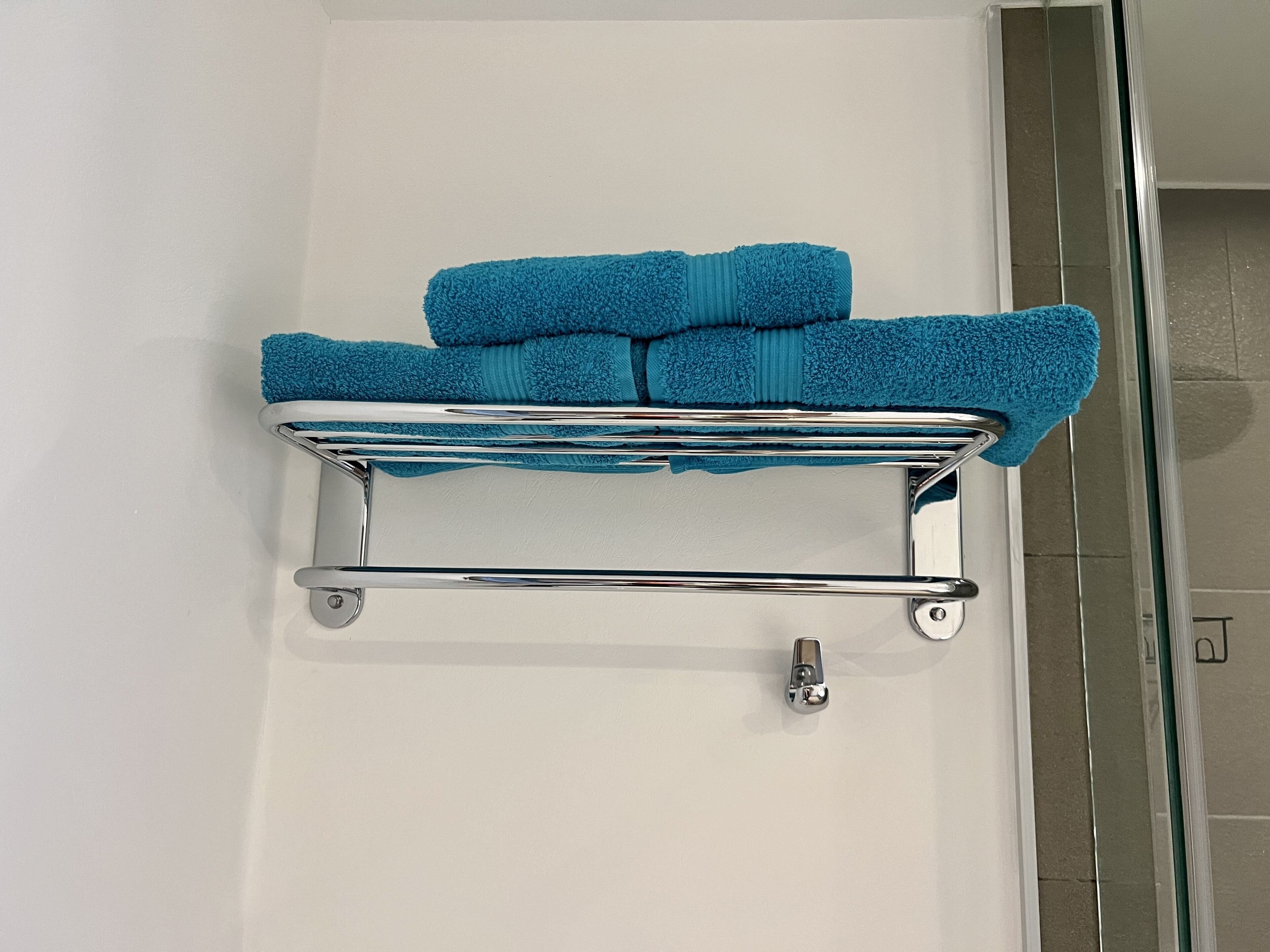 Un baño con un perchero cromado que sostiene dos toallas azules.