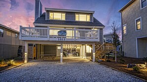 A two-story house with a balcony, a number '1011' sign, and a gravel driveway. - Your Ultimate  Retreat – Steps from Beach with PVT Heated Pool, Slide & Hot Tub! (Surf City)
