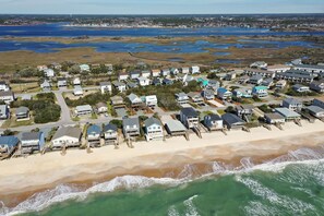An aerial view of a coastal residential area with houses along the beach, a sandy shoreline, and a marshy area with water bodies in the background. - Your Ultimate  Retreat – Steps from Beach with PVT Heated Pool, Slide & Hot Tub! (Surf City)
