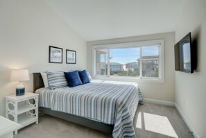 A bedroom with a bed, a nightstand, a lamp, a window with a view of buildings, and a mounted TV.