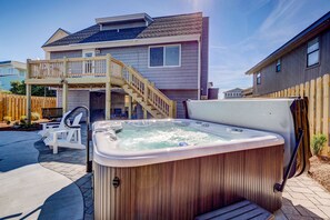 A backyard with a hot tub, wooden deck, and a house with a balcony.