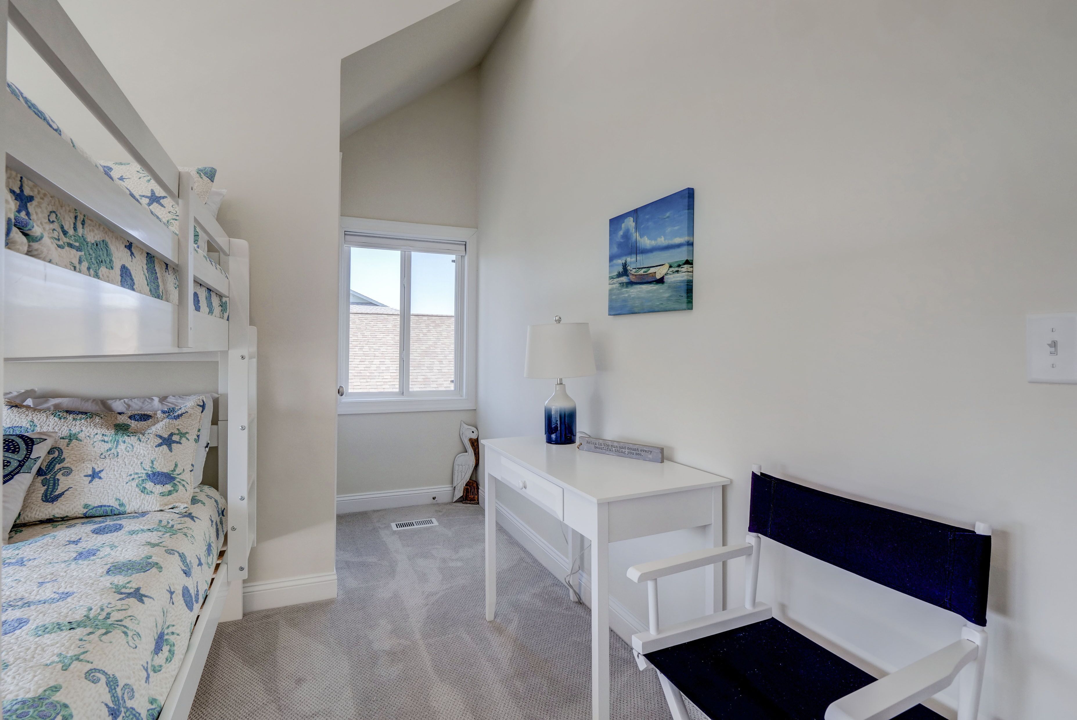 A bedroom with bunk beds, a desk, a chair, a lamp, and a painting.