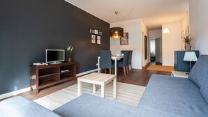 Uma sala de estar moderna com um sofá cinzento, uma unidade de entretenimento de madeira e uma área de jantar com mesa e cadeiras.