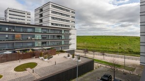 Um edifício moderno com vários andares, um pátio com áreas de estar e vista para uma colina verde.