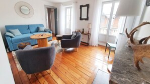Un salon avec un canapé bleu, une table basse ronde, un fauteuil gris et un plancher en bois.