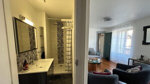 Une salle de bain moderne avec une douche, un lavabo et un miroir. Il y a également un espace de vie avec un canapé et une table basse.