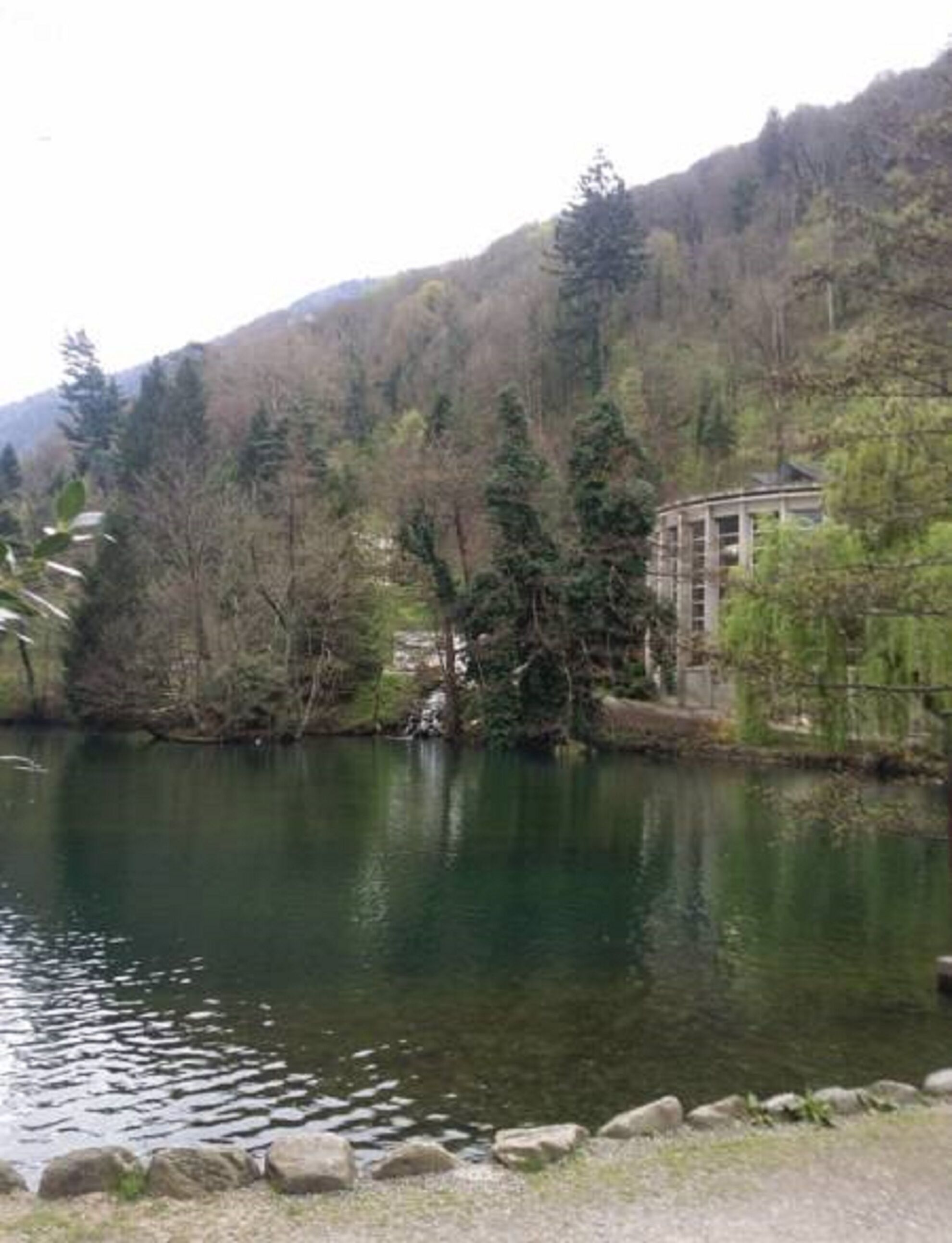 A lake with a building on the right, surrounded by trees and hills.