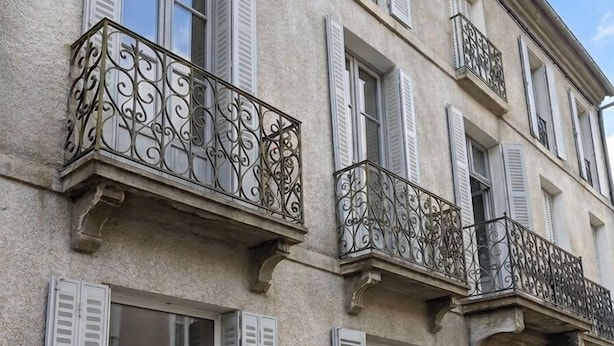 Un immeuble à plusieurs étages, doté de volets blancs, de balcons décoratifs et d’une façade à motifs.
