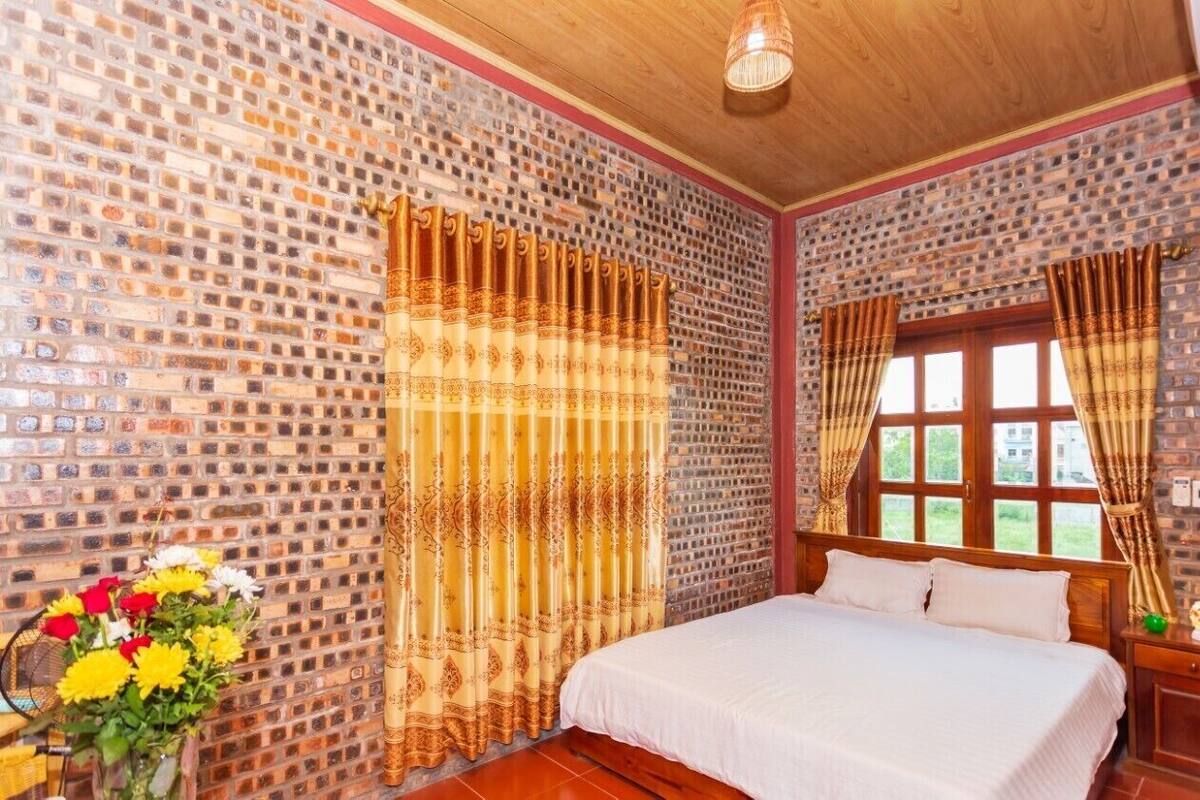 Une pièce avec un mur dont le motif rappelle celui d’un mur en briques, un lit avec une literie blanche et des rideaux à motifs dorés.