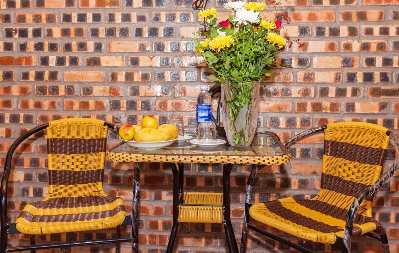 A brick wall with a table and two wicker chairs. A vase with flowers is on the table.