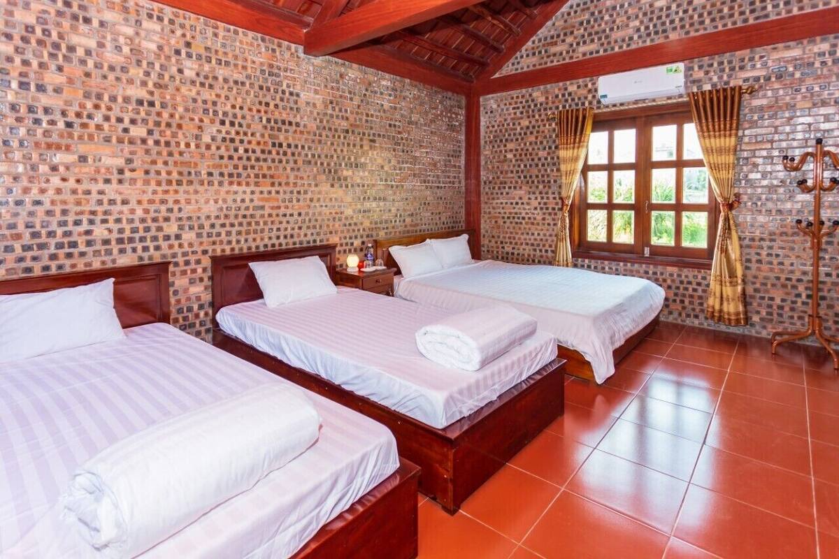 Une chambre d’hôtel avec trois lits en bois, un mur décoré d’un motif en briques, une grande fenêtre avec des rideaux et un plafond en bois.