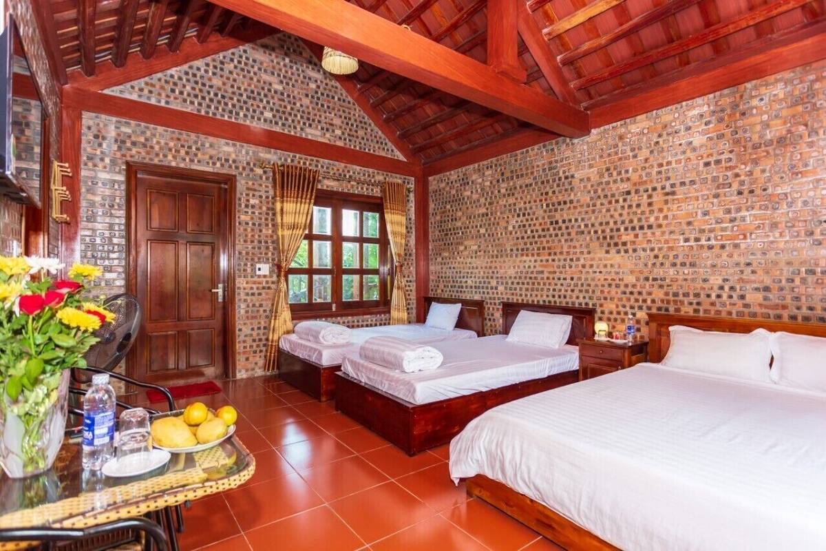 Une chambre d’hôtel avec trois lits, un plafond en bois, un mur décoré d’un motif en briques et une fenêtre avec des rideaux.