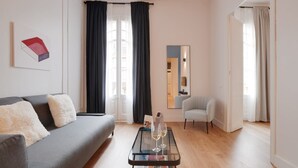 Un salon moderne avec un canapé gris, une table basse en verre sur laquelle sont posés des magazines et un petit fauteuil.