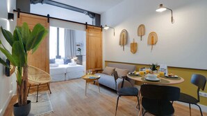 A modern living room with a sofa, dining table, chairs, and a large plant. - Sweett | Sepulveda 3B (Barcelona)