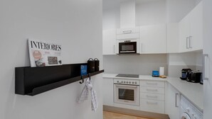 A compact kitchen with white cabinets, a microwave, an oven, and a washing machine. - Sweett | Sepulveda 3B (Barcelona)