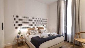 Een moderne slaapkamer met een bed, nachtkastjes, een wandlamp en uitzicht op het landschap door een raam met gordijnen.