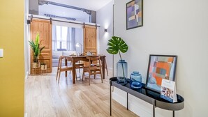 Een moderne woonkamer met een eethoek, houten vloeren, een groot raam en een plant.