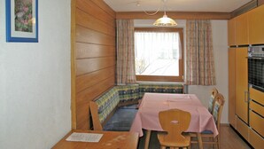 A compact kitchen with wooden cabinets, a dining table with chairs, a bench, and a window with curtains.