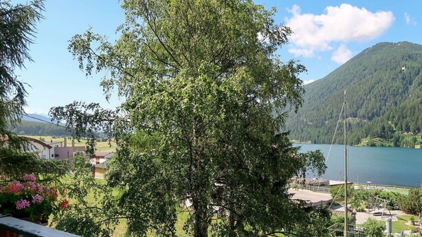 A view of a lake surrounded by mountains, a playground, and a building with a balcony.