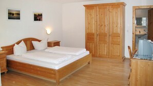 Une chambre à coucher avec un lit en bois, deux tables de chevet, une armoire et une salle de bain visible à travers une porte ouverte.