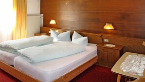 Una cama doble con sábanas blancas, dos lámparas de noche, un cabecero de madera y una mesita de noche, sobre un suelo cubierto de moqueta roja.