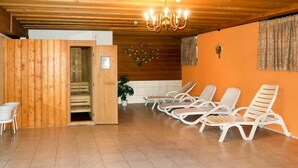 Un cuarto de sauna con paredes y techo de madera, y un candelabro. Se observan sillones blancos y una pequeña mesa con una silla.