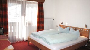 Una cama doble con cabecera de madera, una mesita de noche, un televisor y una ventana con cortinas.