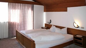 Ein Schlafzimmer mit Holzboden, einem großen Bett mit weißer Bettwäsche, einem Nachttisch und einer wandmontierten Lampe.