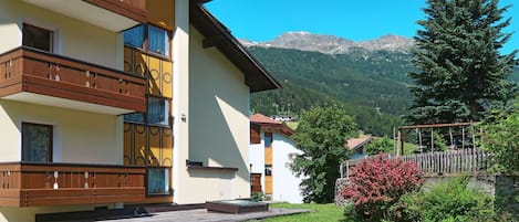 A multi-story building with balconies, a grassy yard, and a mountain backdrop.