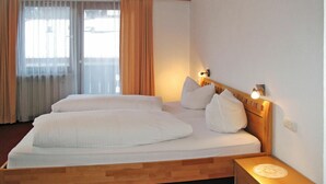 Une chambre d’hôtel avec un lit en bois, du linge de lit blanc, une table de chevet avec une lampe et une fenêtre avec des rideaux.