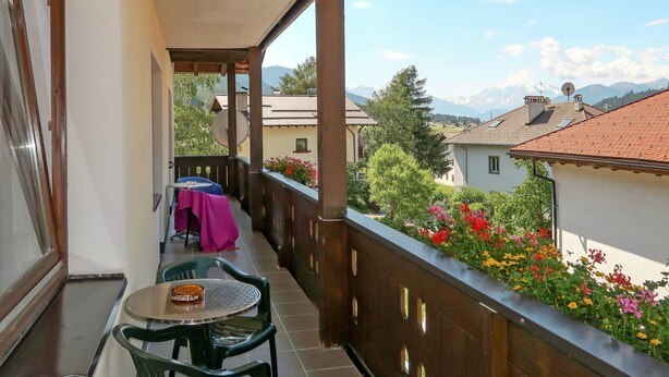Un balcon avec une table et des chaises, une vue sur une chaîne de montagnes et un parterre de fleurs.