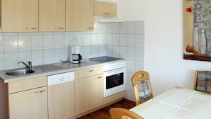 Une cuisine compacte avec des meubles en bois clair, un lave-vaisselle encastré, une cuisinière et une machine à café.