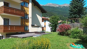 Un edificio de varios pisos con balcones, un patio cubierto de césped y un paisaje montañoso de fondo.