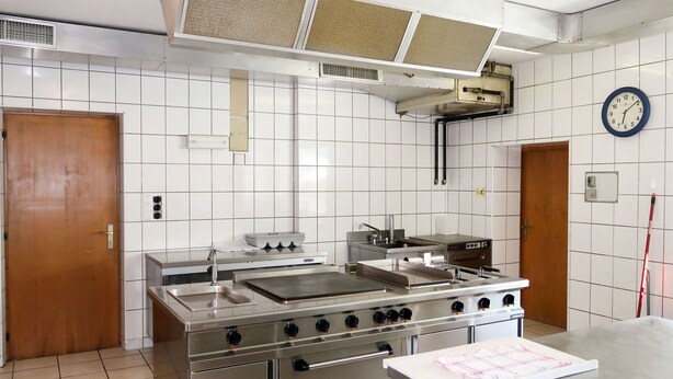 Una cocina comercial con electrodomésticos de acero inoxidable, un reloj y paredes con azulejos.