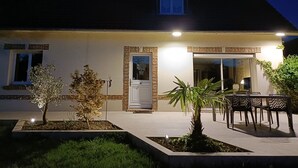 Una casa de dues plantes amb façana de maó, una porta principal i una petita zona de porxo amb una taula i cadires.
