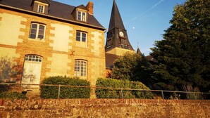 Un edifici històric amb un campanar imponent i una torre del rellotge, envoltat de vegetació exuberant i una paret de pedra.