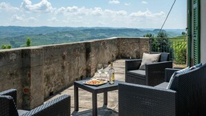 Un balcon agrémenté de meubles en osier, une table où sont servis des plats et des boissons, et une vue sur des collines ondoyantes.