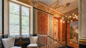 Une pièce dotée d’un escalier, de décorations murales élaborées et offrant une vue sur un bâtiment par une fenêtre.