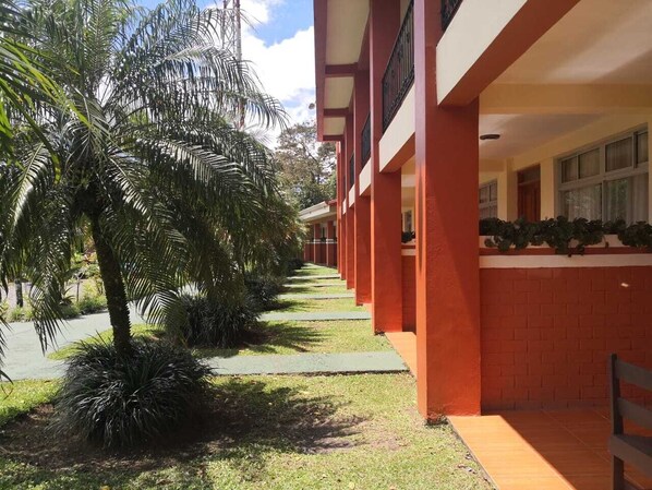 A building with a red facade and a covered walkway lined with palm trees.