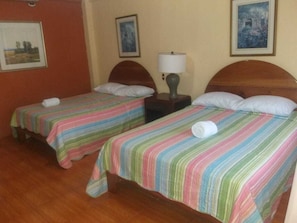 A hotel room with two single beds, each with a striped bedspread and a rolled towel. There is a nightstand with a lamp between the beds. - Arenal Volcano View Rooms (La Fortuna)