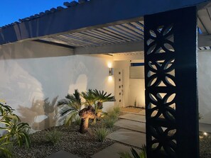 Ein modernes Haus mit überdachter Terrasse, einem dekorativen Metallzaun und einem gut beleuchteten Eingang.