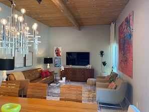 Ein modernes Wohnzimmer mit Holzboden, einem großen Flachbildfernseher, einer Couch, einem Couchtisch und einem Essbereich mit Stühlen.
