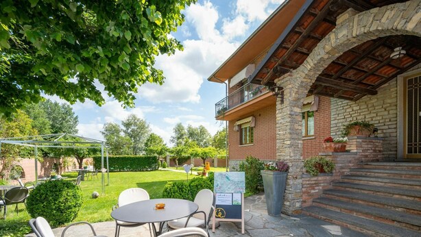 A patio with outdoor seating and a stone pathway leading to a building with a stone facade and a balcony. - Nice apartment for 4 people with WIFI, A/C, pool, TV and patio (Castagnole Delle Lanze)