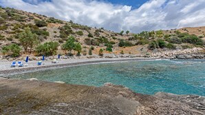 Ein Strand mit klarem türkisblauem Wasser, felsigem Ufer und einigen blauen Liegestühlen.