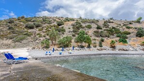Ein Strand mit klarem Wasser, felsigem Ufer und einem Hügel mit vereinzelter Vegetation.