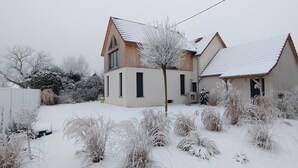 A two-story house with a sloped roof, surrounded by snow-covered vegetation.