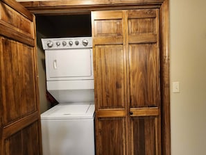 A laundry room with a stacked washer and dryer, wooden cabinets, and a white wall.