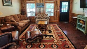 Una sala de estar acogedora con un sofá de cuero marrón, un sillón estampado, una mesa de centro de madera y una alfombra con estampado animal en blanco y negro.